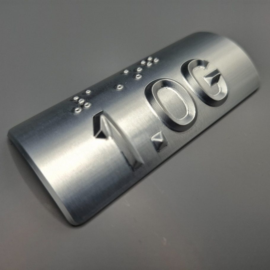 Glatte Metallplatte mit der Prägung "1.0G" und Brailleschrift.